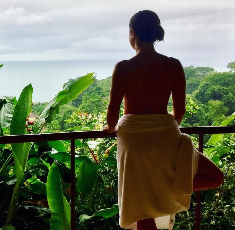 Woman in towel looking over forest and ocean